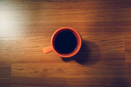 Orange hot coffee mug on the wooden floor in low light room.