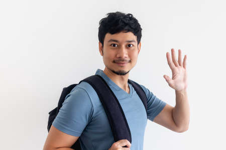 Asian man in blue t-shirt with backpack is waving hand on isolated background.の写真素材