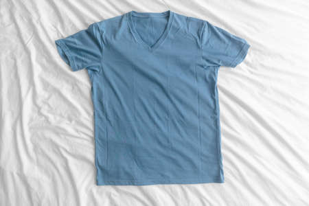 Blue simple t-shirt lie on white bed sheet.の写真素材