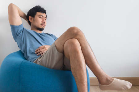 View of mans legs on white bed with TV and plant. Concept of relaxation.