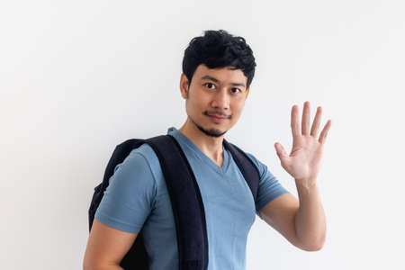 Asian man in blue t-shirt with backpack is waving hand on isolated background.の写真素材