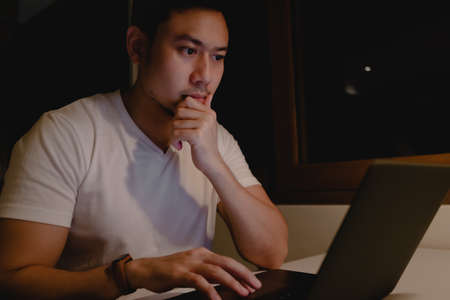Serious Asian man is working with laptop at night. Concept of work hard and late.