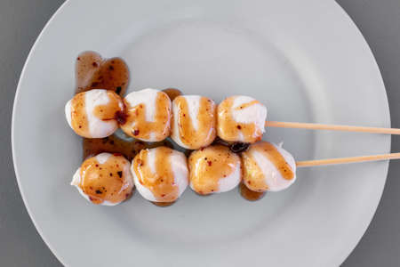 Two Thai pork balls stick with spicy and sweet sauce on white dish.