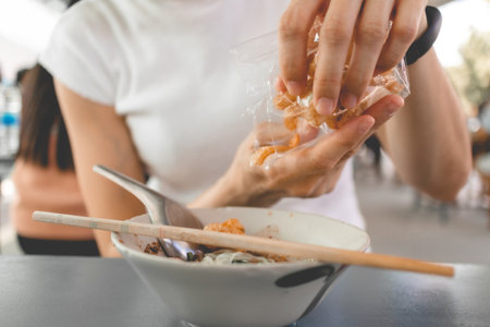 Woman in white t-shirt eats pork rind or pork crackling with Thai noodle.