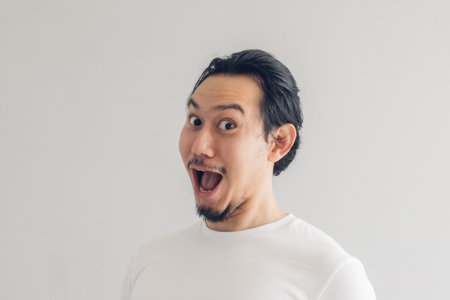 Funny grinning smile face of Asian man in white t-shirt and grey background.の写真素材
