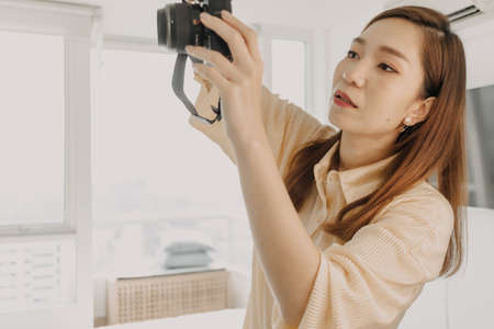 Asian woman photographer checking the camera viewfinder in her own apartment.