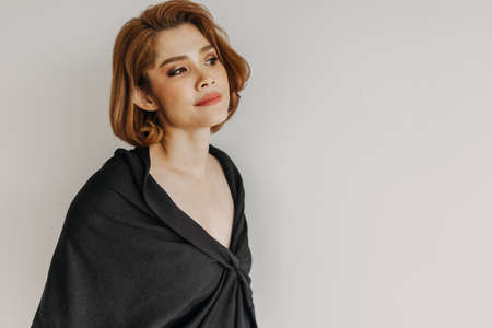 Cool looking Asian woman wears a black dress and white wall background.