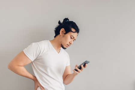 Long hair Asian man in white casual t-shirt is using smartphone.の写真素材