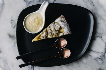 Close up of Apple Crumble Cake with custard on dark table in the cafe.