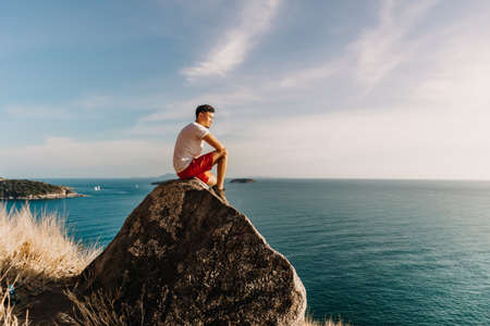 Asian man rest on the sea cliff rock after finish his hike trail.の写真素材