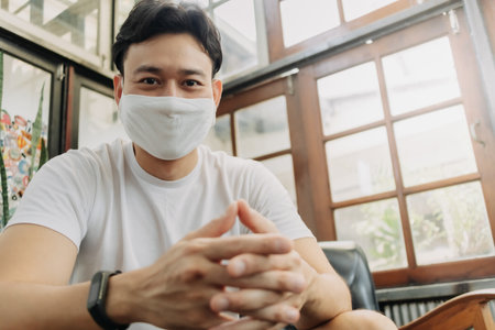Asian man influencer with mask is talking with his camera in a cafe.の写真素材