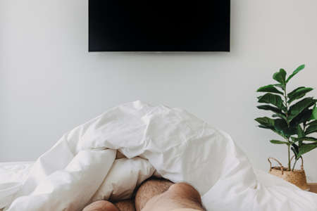 Person sleeping on white bed and watching television. Concept of stay at home.の写真素材