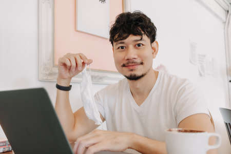 Happy Asian man work in a cafe taking off mask and smile.
