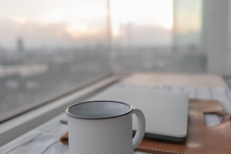 Laptop and white coffee cup with city view from apartment. Concept of work from home.の写真素材