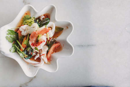Thai seafood spicy salad served in a fancy bowl on white table.の写真素材
