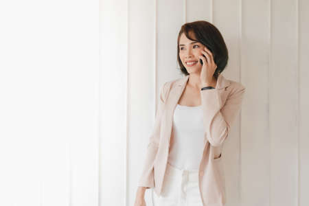 Happy Asian working woman is having smartphone conversation on white background.の写真素材