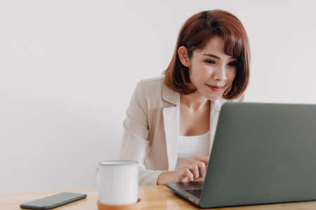 Pretty happy Asian working woman is working on her laptop in the office.の写真素材