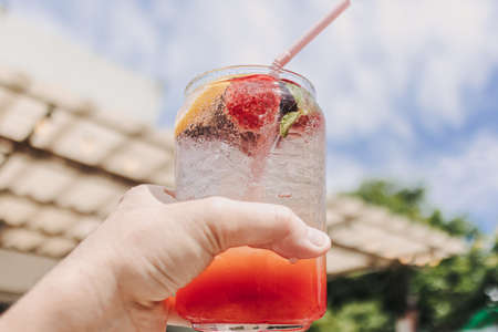 Hand holding Mixed Fruits Pink Italian soda against sunny sky of summer.の写真素材