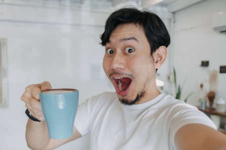 Happy Asian man enjoy his coffee and selfie himself with his coffee cup.の写真素材