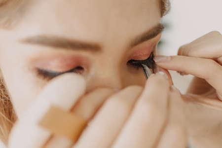 The makeup artist is applying makeup on client eyes.