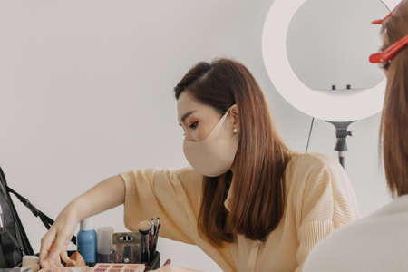 Asian woman makeup artist is at work and wearing makeup on her model.
