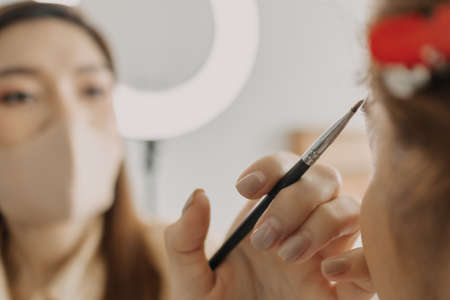 Asian woman makeup artist is at work and wearing makeup on her model.の写真素材