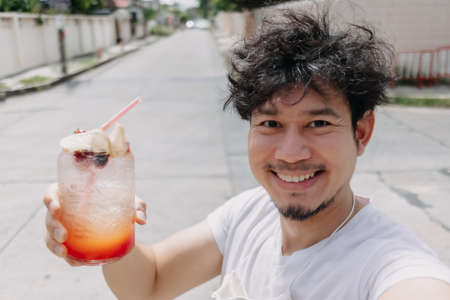 Happy funky hair Asian man drinks Italian soda syrup in hot sunny street of summer.の写真素材