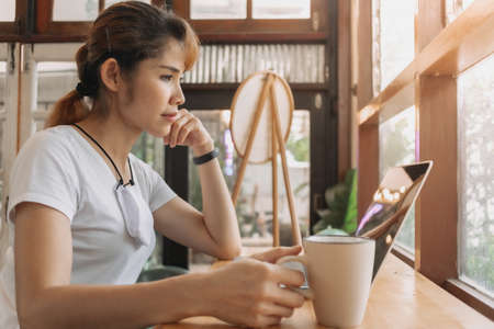 Asian woman is working in coffee cafe with face mask on her neck.の写真素材