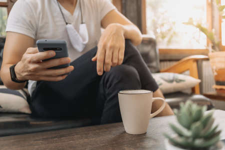 Asian man with mask is using smartphone and drink coffee in the cafe.の写真素材