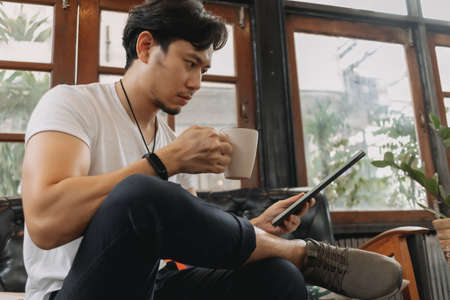 Asian man work in a living room with tablet and coffee. Concept of staycation.