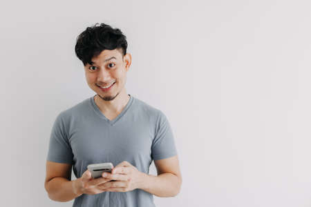 Smile Asian man is happy with the smartphone application isolated on white wall.の写真素材