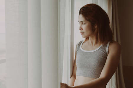 Attractive Asian woman look at the view behind the curtain in the hotel.の写真素材