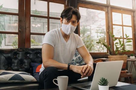 Asian man wearing face mask is working with laptop in a cafe.の写真素材