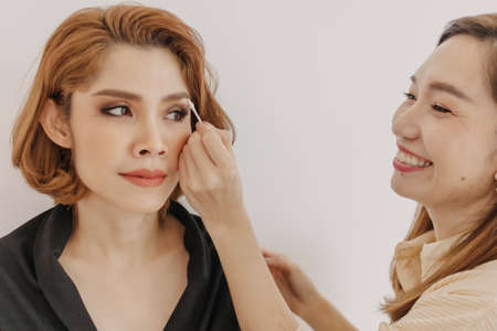 Asian woman makeup artist is at work and wearing makeup on her model.の写真素材