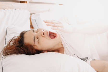 Funny sleepy yawning Asian woman just wake up on her bed.
