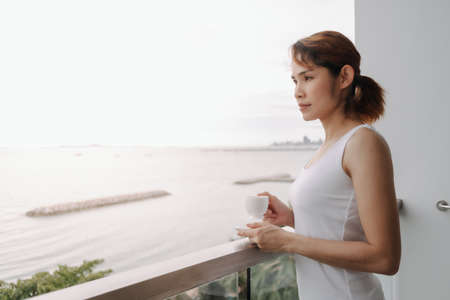 Asian woman drink coffee and relax on the balcony with sea view.