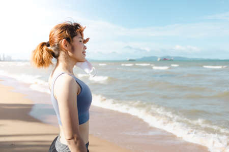 Asian woman take off mask and rest after finish jogging by the beach in summer.の写真素材