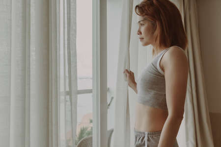Attractive Asian woman look at the view behind the curtain in the hotel.の写真素材
