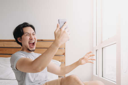 Shocked and happy Asian man get good news from the smartphone.