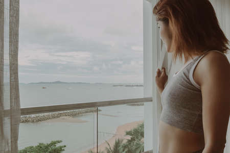 Attractive Asian woman look at the view behind the curtain in the hotel.の写真素材