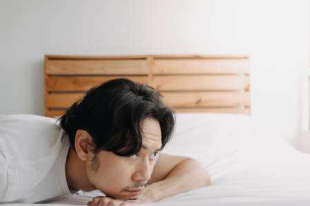 Exhausted Asian man lay on the bed as he feels burnout.の写真素材