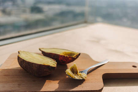 Sweet potato cut into half serve with teaspoon on wooden board.