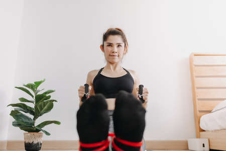 Asian woman in sport wears do Resistance Band Seated Pronated Row in her room.