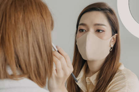 Asian woman makeup artist is at work and wearing makeup on her model.の写真素材