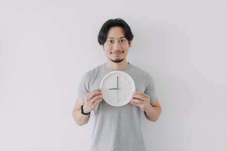 Smile face asian man in grey t-shirt holding a white clock. Concept of time.の写真素材