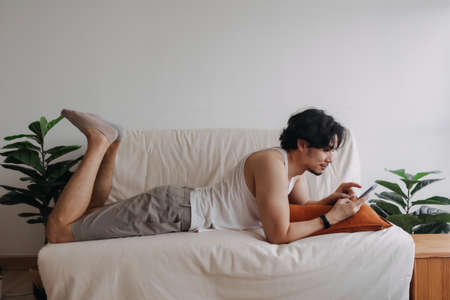 Bored Asian man relaxed and use smartphone for killing time alone in apartment.の写真素材