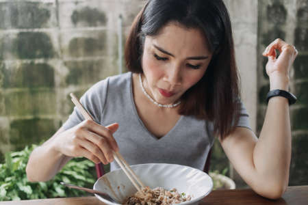 Asian woman eat spicy noodles with chopsticks in local street.の写真素材