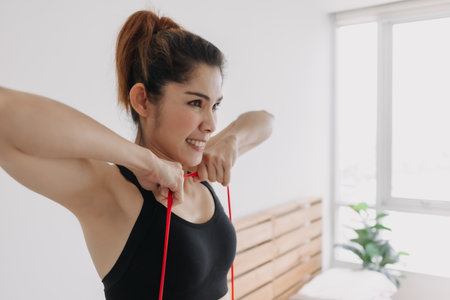 Asian woman in sport wears do Resistance Band Upright Row workout in bedroom.