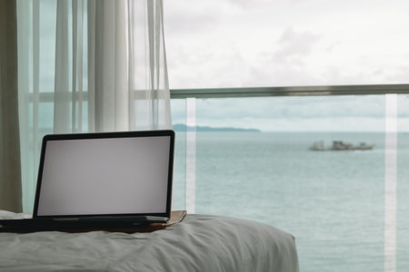 Workation concept. Empty screen laptop on bed with ocean view balcony.の写真素材