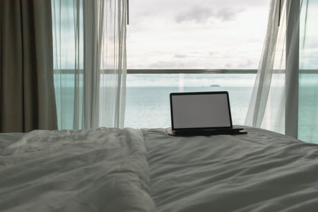 Workation concept. Empty screen laptop on bed with ocean view balcony.の写真素材